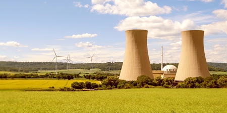 Grüne Landschaft mit Kernkraftwerk und Windrädern im Hintergrund