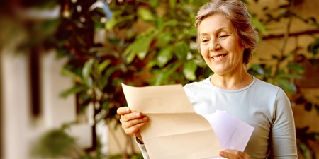 Glückliche ältere Frau zu Hause, die einen Brief liest, den sie in der Post bekommen hat und lächelt.